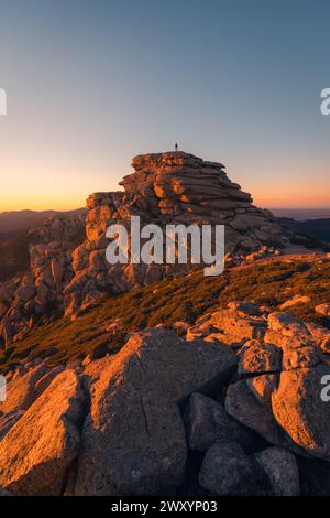 Une vue sereine de Siete Picos dans la Sierra de Guadarrama, se prélasser dans la lueur chaude de l'heure dorée, avec une personne solitaire au sommet des rochers Banque D'Images