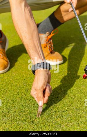 Vu d'en haut, un golfeur méconnaissable répare le gazon sur un parcours de golf luxuriant, contrastant avec le style traditionnel du sport. Banque D'Images