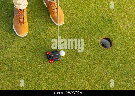 D'en haut, un golfeur méconnaissable, arborant une paire unique de bottes brunes, est sur le point de putter une balle de golf dans le trou pendant un jeu tranquille de Banque D'Images