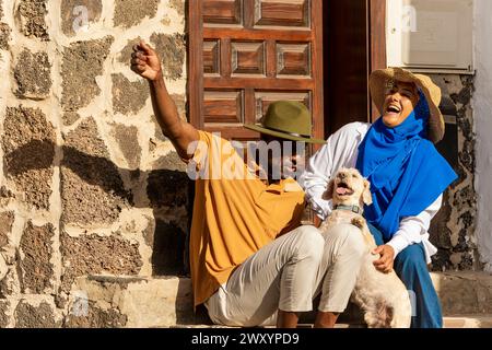 Un joyeux couple multiethnique est assis sur les marches extérieures, partageant un moment de joie avec leur adorable chien Banque D'Images