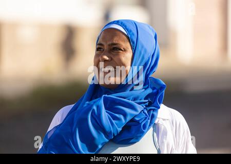 Une femme multiethnique souriante portant un hijab bleu et un vêtement blanc pose à l'extérieur avec un fond de flou Banque D'Images