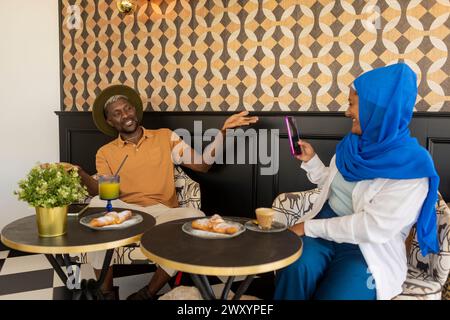 Un homme et une femme profitent d'une conversation allégée dans un café, avec des boissons et des pâtisseries sur leur table Banque D'Images