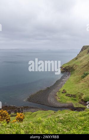 Surplombant les eaux sereines de l'île de Skye, le littoral près de Lealt Falls révèle une falaise verdoyante descendant vers un rivage de galets Banque D'Images