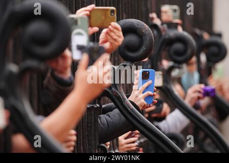 Les membres du public utilisent leur téléphone pour filmer et photographier la bande des gardes gallois lors de la cérémonie de relève de la garde au Palais de Buckingham, à Londres, alors qu'ils interprètent l'hymne de l'OTAN pour célébrer le 75e anniversaire de l'Organisation du Traité de l'Atlantique Nord. Date de la photo : mercredi 3 avril 2024. Banque D'Images