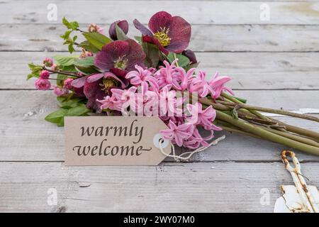 Bouquet avec jacinthes roses, roses de Noël et carte avec texte anglais : chaleureusement bienvenue Banque D'Images