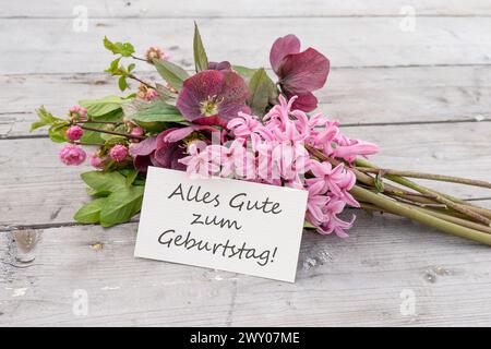 Carte de voeux avec bouquet de jacinthes bleues et carte avec texte allemand : joyeux anniversaire Banque D'Images