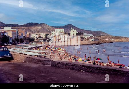 Plage de San Sebastian à Sitges, Espagne, en août 1965. Bâtiments en bord de mer non aménagés avec église Ermita de San Sebastián au-delà. Platja de Sant Sebastià Banque D'Images