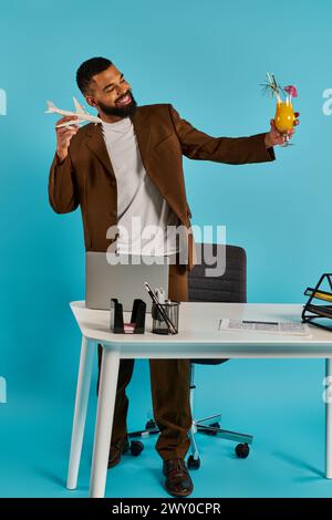Un homme est assis à un bureau en bois, tenant sereinement un verre de jus d'orange fraîchement pressé. Banque D'Images