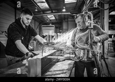 Deux ouvriers, un jeune et un aîné, effectuent le soudage par points de tôles d'acier dans un atelier de fabrication. Banque D'Images