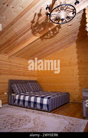La chambre est décorée avec des lambris de bois chaleureux et un lit doux et accueillant. Un beau lustre fournit un éclairage doux. Banque D'Images