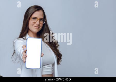 Altina jeune femme souriante floue avec la main tendue montrant avec sa main écran blanc de téléphone, focus sur le téléphone, studio shot avec backgrou blanc Banque D'Images