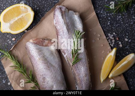 merlu de poisson assaisonné avec des herbes, du poivre et du citron sur une planche de bois rustique, pour des recettes ou des étalages de marché de fruits de mer Banque D'Images