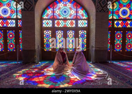 Shiraz, Iran - 29 février 2024 : la mosquée Nasir al-Mulk, également connue sous le nom de mosquée rose, les femmes locales se tiennent devant le vitrail coloré. Banque D'Images