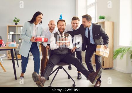 Joyeux homme heureux célébrant son anniversaire au bureau avec ses collègues. Banque D'Images