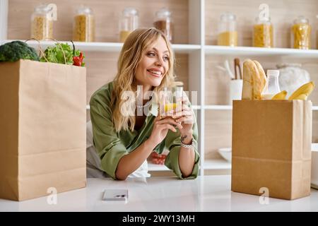 Femme assise à la table de la cuisine de l'appartement, tenant un verre de jus d'orange. Banque D'Images