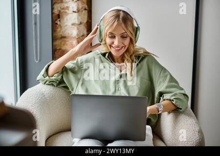 Femme assise dans une chaise à la maison, utilisant un ordinateur portable et portant des écouteurs. Banque D'Images