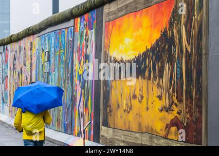 Berlin, Allemagne. 3 avril 2024. Une scène apocaliptique est passée par quelqu'un aux couleurs ukrainiennes avec des parapluies et des imperméables par temps pluvieux - la East Side Gallery à Berlin. Un projet de graffiti conservé par 118 artistes couvrant une partie du mur de Berlin et célébrant sa disparition. Crédit : Guy Bell/Alamy Live News Banque D'Images