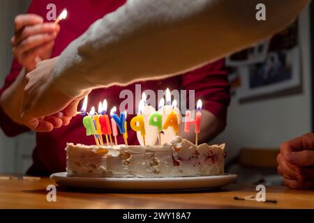 mains avec allumettes allumant des bougies vax sur le gâteau d'anniversaire Banque D'Images