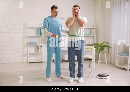 Nutritionniste masculin mesurant la taille de l'homme en clinique Banque D'Images