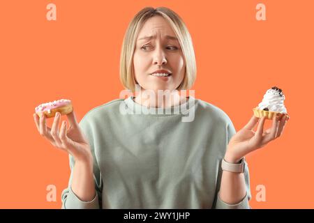 Femme mature réfléchie avec des friandises sur fond orange. Concept de suralimentation Banque D'Images