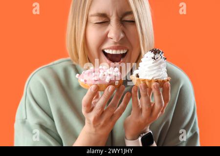 Belle femme avec des friandises sur fond orange, gros plan. Concept de suralimentation Banque D'Images