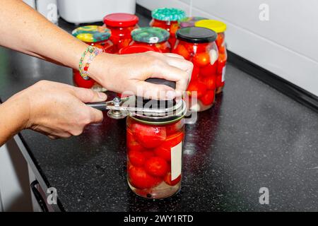 Une femme serre les couvercles sur un pot de tomates marinées rouges avec une sertisseuse. Conservation des légumes. Banque D'Images