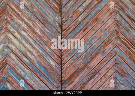 les vieilles planches en bois portent la texture du motif chevron avec des couches de peinture marron et bleue pelées sous une couche de peinture bleue blanchie par le soleil Banque D'Images