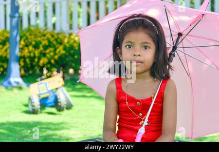 Une jeune fille dans une robe rouge vif saute à travers un parc, tenant un parapluie coloré. Parfait pour les concepts de printemps et d'été. Banque D'Images