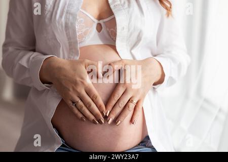 Gros plan du ventre d'une femme enceinte attendant un bébé avec des mains formant un cœur sur le ventre Banque D'Images