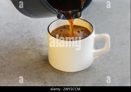 Verser le café d'une cafetière dans une tasse sur un fond blanc Banque D'Images