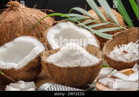 Noix de coco fraîches ouvertes avec des tranches de noix de coco, des flocons et des feuilles de noix de coco sur une table en bois. Joli fond de fruits pour vos projets. Banque D'Images
