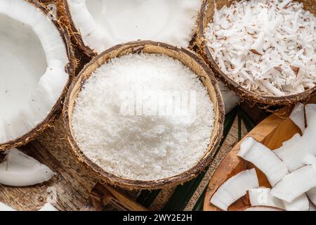 Noix de coco fraîches ouvertes avec des tranches de noix de coco, des flocons et des feuilles de noix de coco sur une table en bois. Joli fond de fruits pour vos projets. Banque D'Images