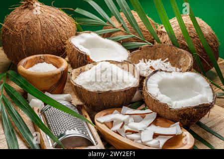 Noix de coco fraîches ouvertes avec des tranches de noix de coco, des flocons et des feuilles de noix de coco sur une table en bois. Joli fond de fruits pour vos projets. Banque D'Images