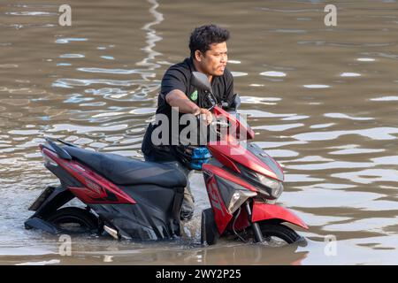 SAMUT PRAKAN, THAÏLANDE, 11 février 2024, Un homme pousse une moto dans une rue inondée, Thaïlande Banque D'Images