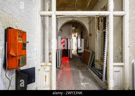 Un vieux téléphone payant orange et un couloir à l'intérieur du bâtiment Infirmiry/Exam à l'hôpital psychiatrique de London, Ontario, Canada. Banque D'Images