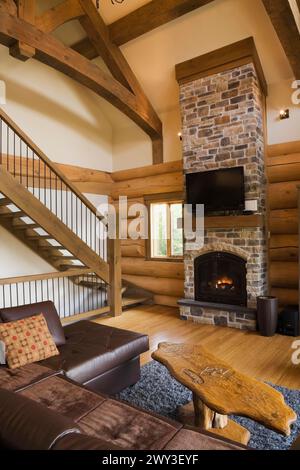 Canapé en l en cuir marron et table basse en bois devant un foyer au propane en pierre naturelle brune et bronzée nuancée à côté d'escaliers en bois Banque D'Images