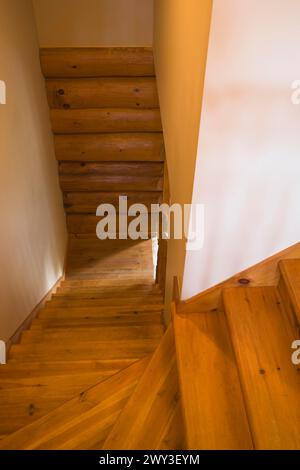 Escalier étroit en bois de pin escarpé et torsadé avec marches naturelles teintées et mur rustique en rondins menant au rez-de-chaussée dans un style scandinave Banque D'Images