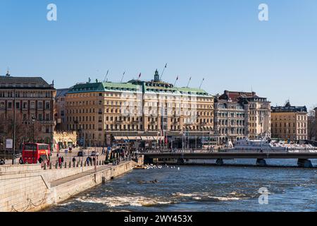 La vieille ville de Stockholm et le centre-ville de stockholm. Le Grand Hotel, drapeaux suédois, pont Strömbron. Lumière du soleil éclatante, printemps. Ciel bleu. Banque D'Images