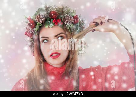 Portrait d'une femme avec une couronne de sapin avec des cônes sur sa tête, tient dans sa main une buse pour une procédure cosmétique sur fond de flocons de neige. Levage RF Banque D'Images