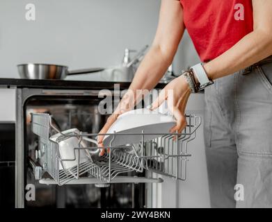 Jeune femme sort la vaisselle propre du lave-vaisselle en gros plan Banque D'Images