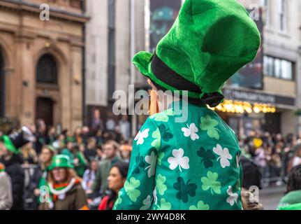 Un enfant portant un chapeau de leprechaun s'assoit sur les épaules des parents pour avoir une bonne vue de la procession au défilé de la St Patrick à Londres. Banque D'Images