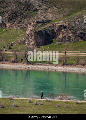 Athlète masculin courant sur un sentier le long de la rive d'une rivière pittoresque. Temps ensoleillé au début du printemps. Beau paysage environnant avec des collines rocheuses Banque D'Images