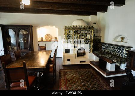 Bran, Brasov, Roumanie- juin, 2023 : élégante salle à manger vintage avec une grande table en bois, cheminée en céramique ornée et meubles anciens. Banque D'Images