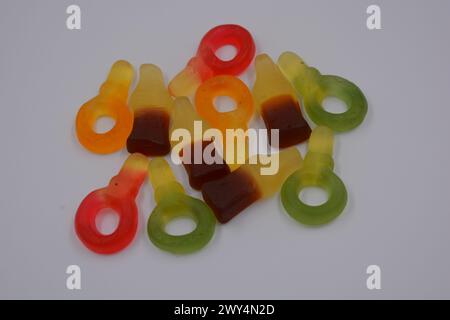 Bonbons beaux et inhabituels. Jaune-vert, rouge, brun, bonbons sous la forme d'une bouteille de Coca-Cola, touches de couleur disposées sur un backgro en plastique blanc Banque D'Images