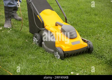 Jardinier en bottes en caoutchouc noir taillant la pelouse avec la tondeuse Banque D'Images