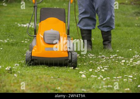Jardinier en bottes en caoutchouc noir taillant la pelouse avec la tondeuse Banque D'Images