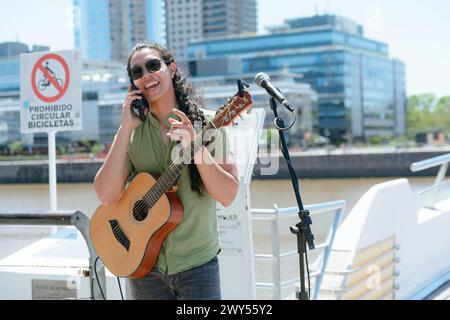 jeune homme musicien guitariste avec de longs cheveux et des lunettes de soleil, debout dans la rue avec sa guitare souriant et parlant au téléphone avant de jouer, copiez l'espace Banque D'Images