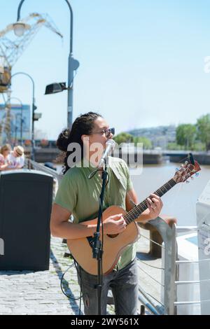 Image verticale d'un jeune homme latino d'ethnie vénézuélienne busker avec de longs cheveux et des lunettes, travaillant à la guitare et chantant à Puerto Madero Arge Banque D'Images