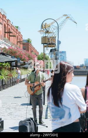 Image verticale d'un jeune homme latino d'ethnie vénézuélienne busker avec de longs cheveux et des lunettes, travaillant à la guitare et chantant à Puerto Madero Arge Banque D'Images