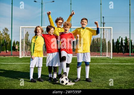 Un groupe animé de jeunes garçons se dresse triomphalement au sommet d'un terrain de football dynamique, se délectant de leur victoire sous le soleil doré. Banque D'Images